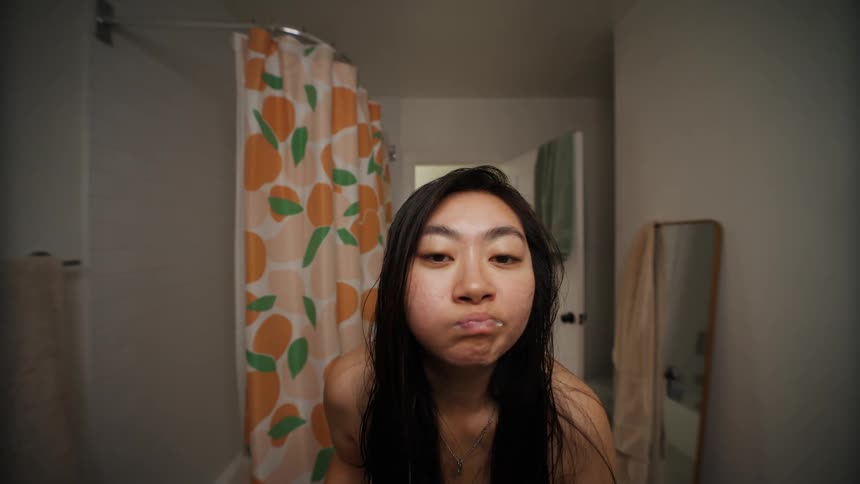 Close up of a woman brushing her teeth in a bathroom mirror then rinsing with water and toweling her mouth off