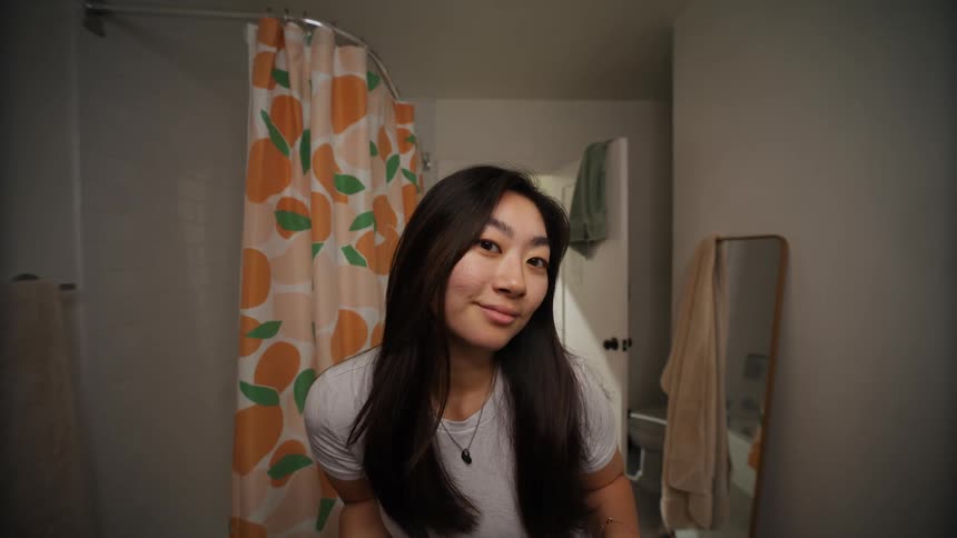An asian woman in the bathroom fixing her hair as she smile to the mirror