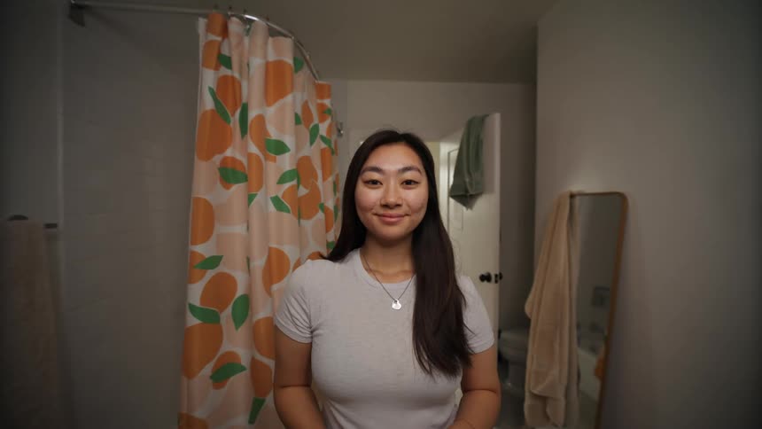 A young woman adjusts her hair until shes happy with how it looks then smiles and leaves the bathroom