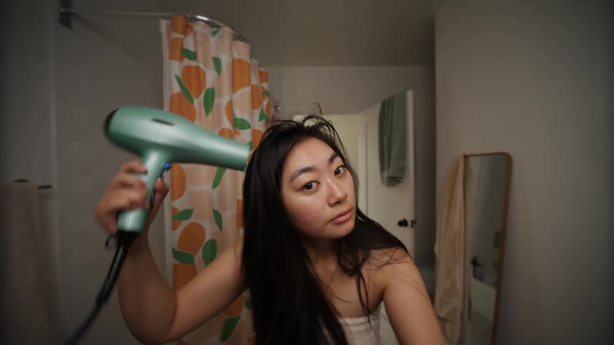 A young woman using a hairdryer to dry her long hair