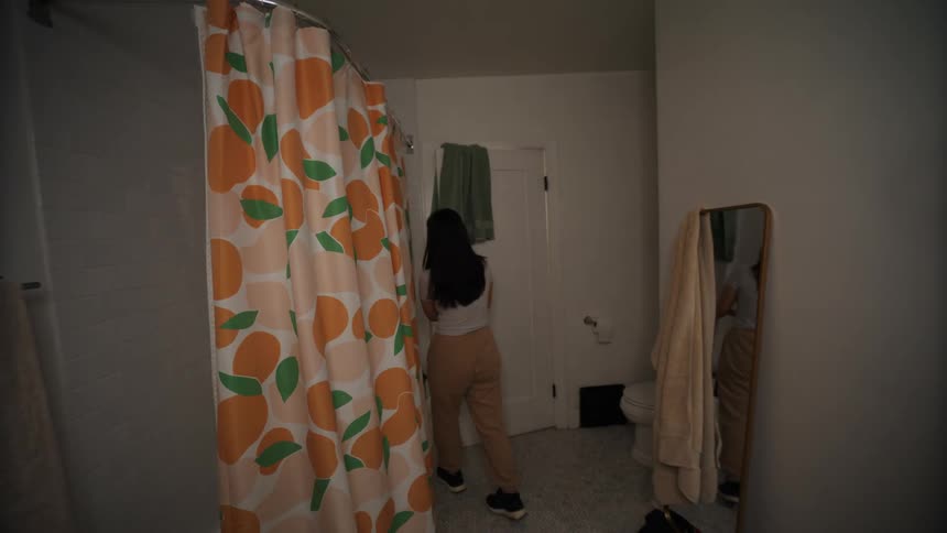 Friends interrupts a woman checking her face on the bathroom mirror