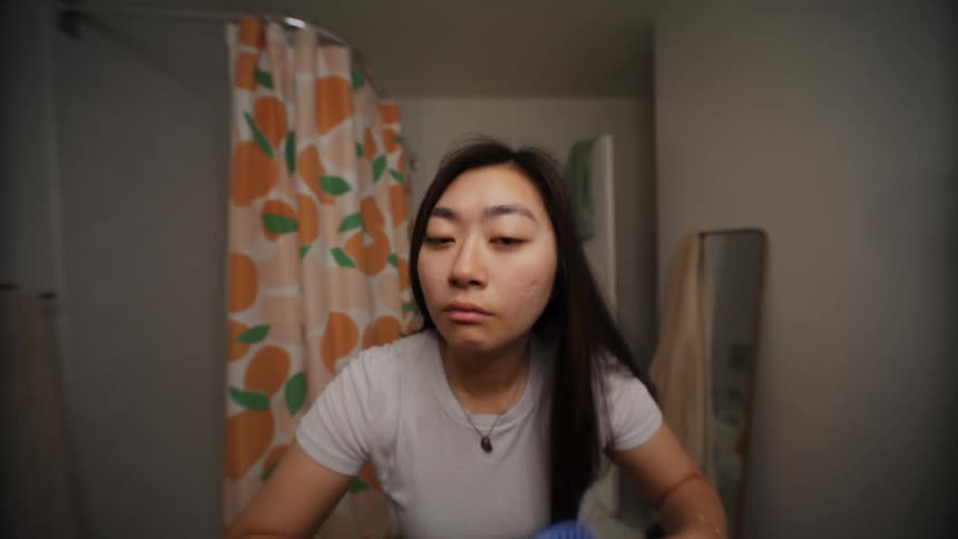 An asian woman looks at herself in the mirror while brushing her hair