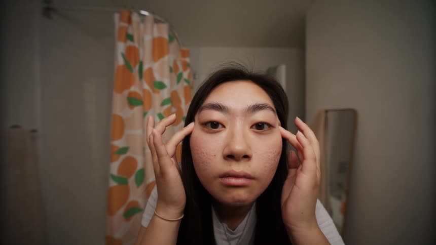 Woman looking in the mirror and rubbing her face with her hands