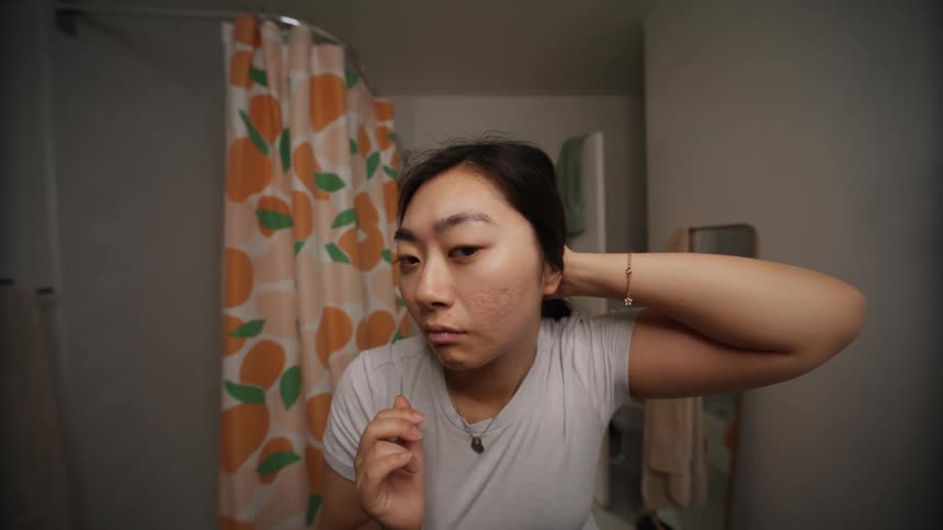 Woman pulls her hair up to check her face on a mirror