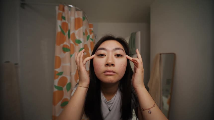 Asian woman indoors adjusting her eyebrows and taking care of her skin in a bathroom