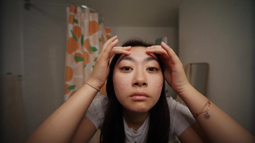 Young woman inspects her face in front of a mirror at home