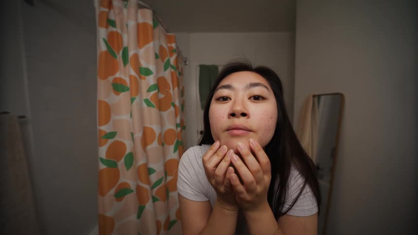 Woman evaluating the skin of her face in a mirror in the bathroom