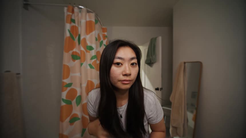 A young asianwoman looks at herself in the mirror while running fingers through her hair
