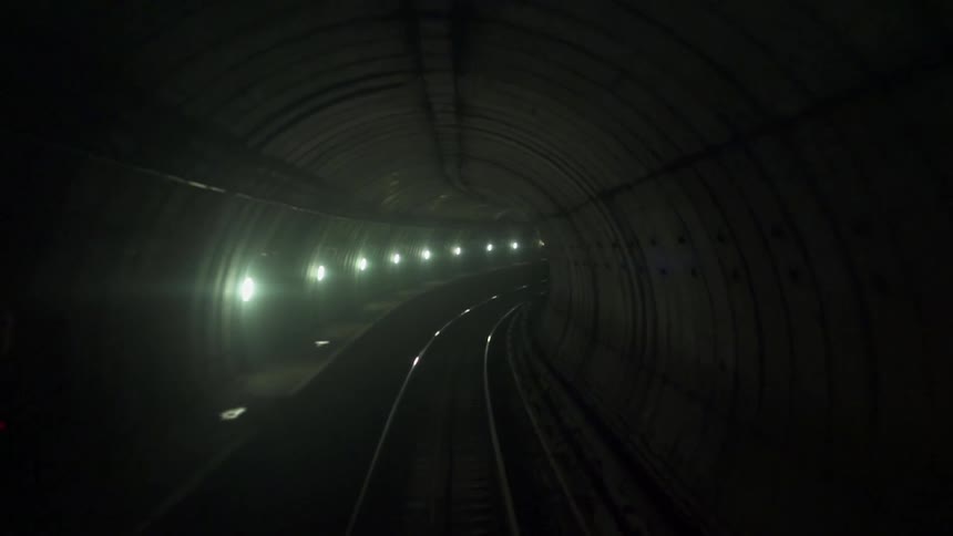 A dark tunnel has a train track running through