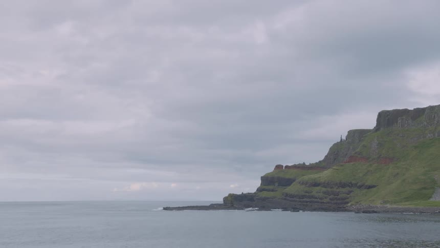 An outline of a view of the sea close to a cliff covered with tiny green grasses on a cloudy day