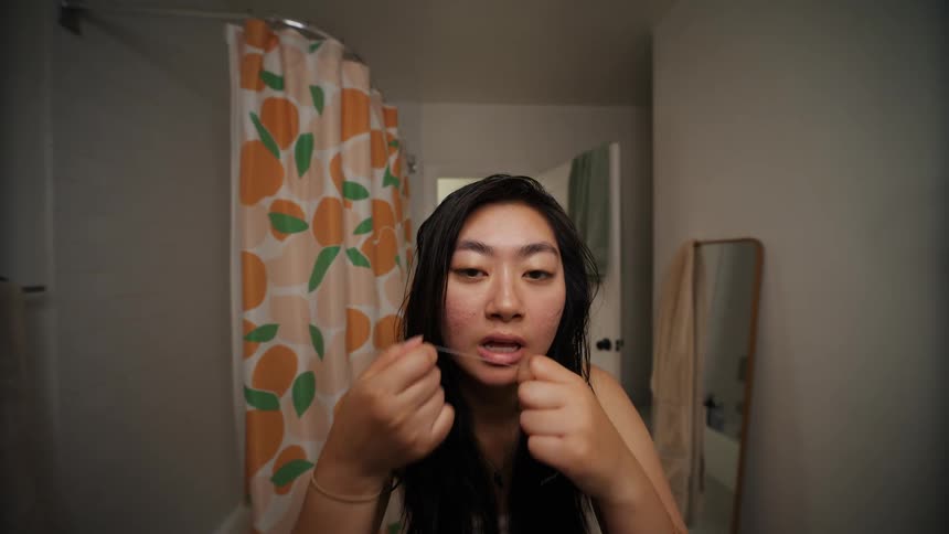 A woman inside the bathroom using a piece of wire to pick her teeth