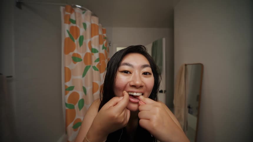 A young woman leans forward and looks into a mirror while flossing