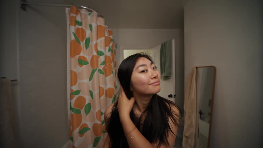 Close up of a woman wearing a towel in the bathroom while brushing her hair and smiling