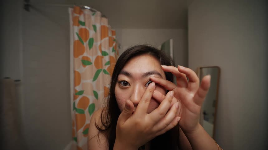 Young woman putting on contact lenses in bathroom at home