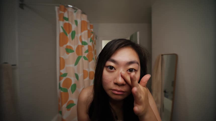 Asian woman indoors applying contact lenses on a bathroom