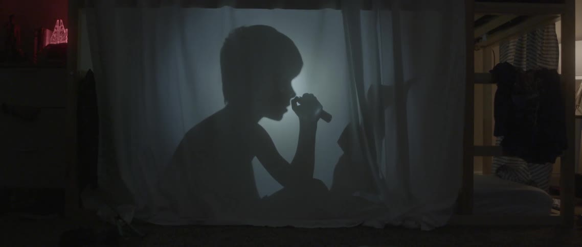 Silhouette of a young boy using a flashlight to read behind some cloth