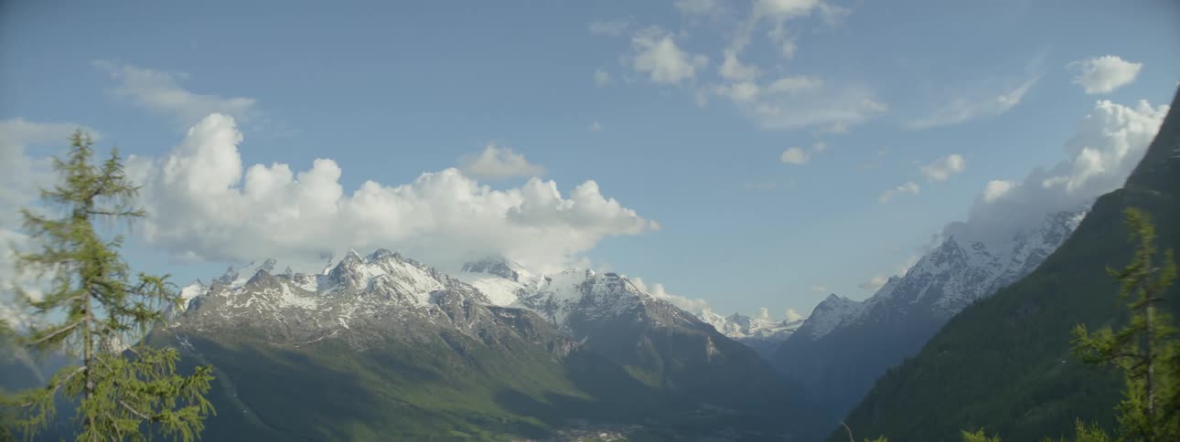 Snow covered mountain peaks on a mountain range with fluffy clouds in the sky above