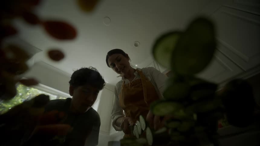 Son leans down to watch mothers hands as she slices vegetables