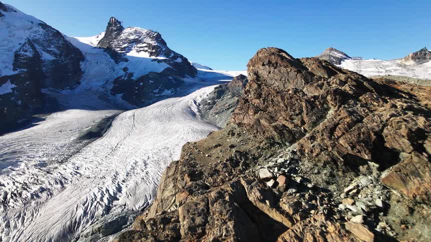 A view of a rocky mountain and another mountain covered with snow on a sunny day
