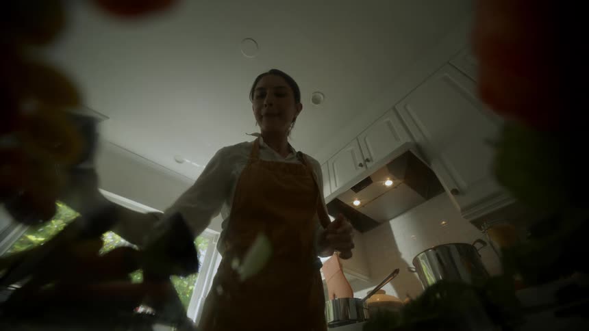 A woman wearing an apron preparing food in her kitchen moving food around on the counter