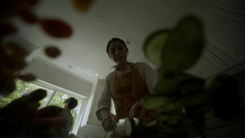 The mother cuts vegetables with a knife while her son walks around in the kitchen