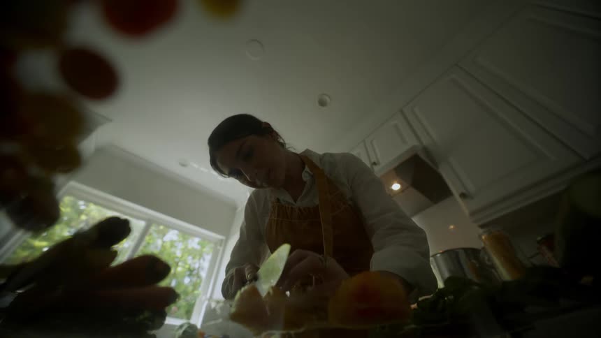 Woman wearing apron holds citrus fruit while slicing it