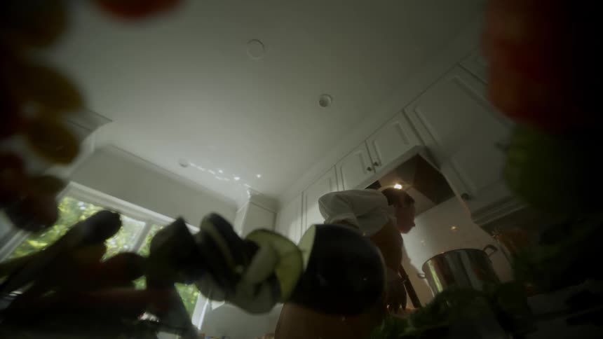 Point of view from a counter top of a woman cooking and preparing food around her kitchen