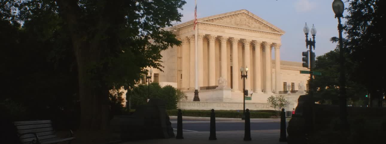 Two trees stand on each side framing the view of the supreme court while a person jogs right past it in the middle of the street