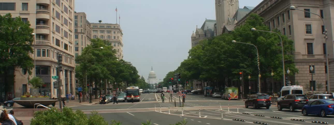 Pedestrians and vehicles move through intersection of road leading toward capitol building