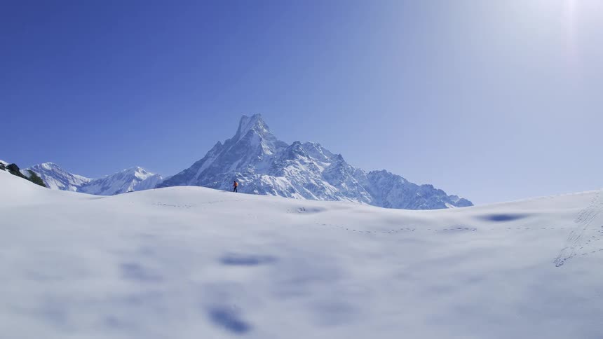 Aerial of man hiking on snowy mountain with distant mountain ridge in the background under the shining sun