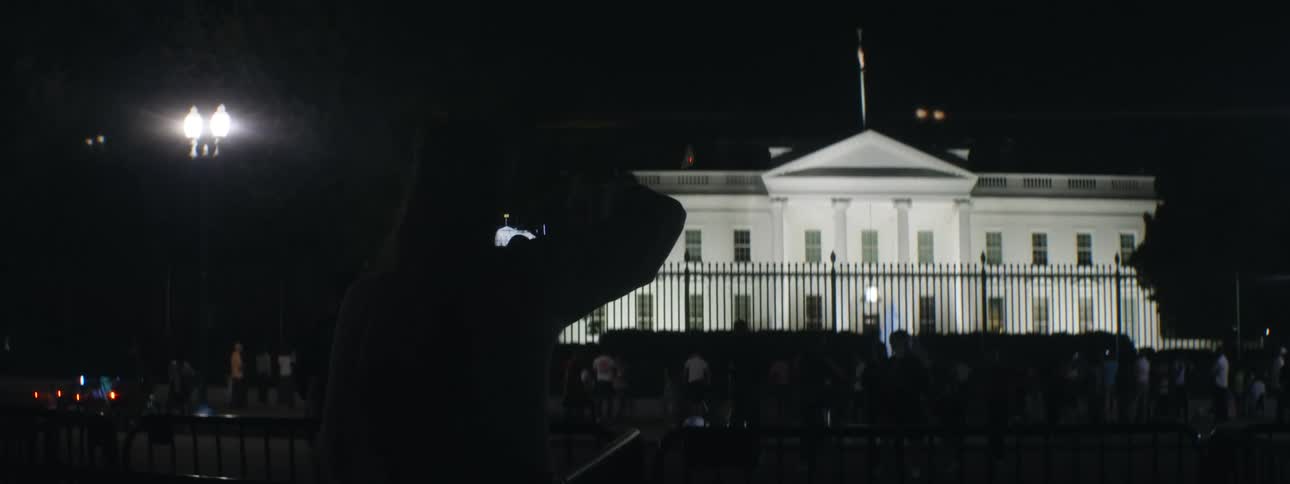 People gathered in front of the white house in the middle of the night with low lighting
