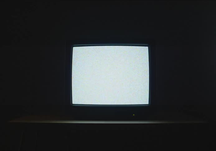 A small old television screen with white and gray static on the screen on a table in a dark room