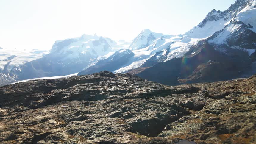 A hilly terrain with rough features located near a mountain where the snow is melting on a sunny day