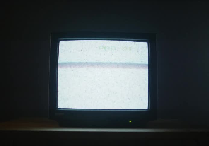 A television set in darkness with changing channels on the screen