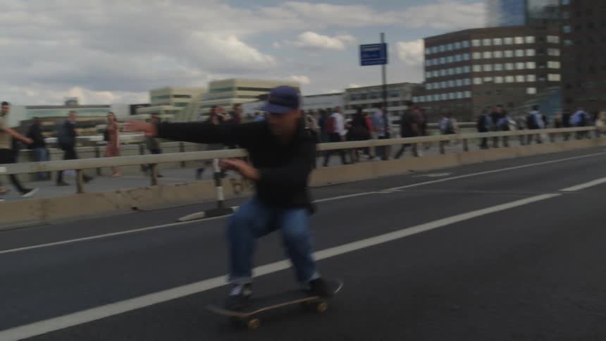 People walking on a city sidewalk as bicyclists and skateboarders ride by on the road near public transportation