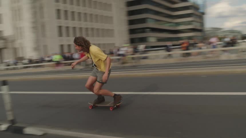 A man skateboards down a busy city street with people cycling on the opposite side and a large crowd of people walking