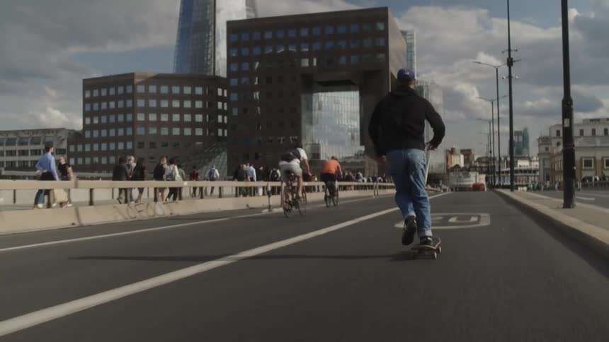A young man riding a skateboard on an empty street and several people passing by on bicycles