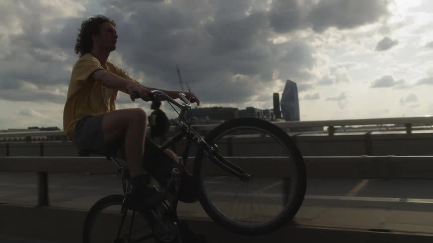 Cyclist performs extended wheelie on bicycle as he rides across one of several bridges in the city on cloudy day