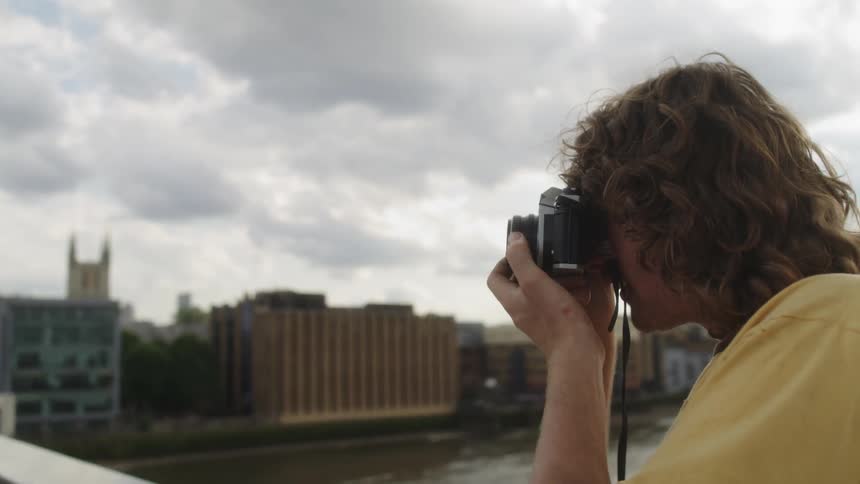 Photographer smiles while taking pictures across river from mid rise buildings on overcast day