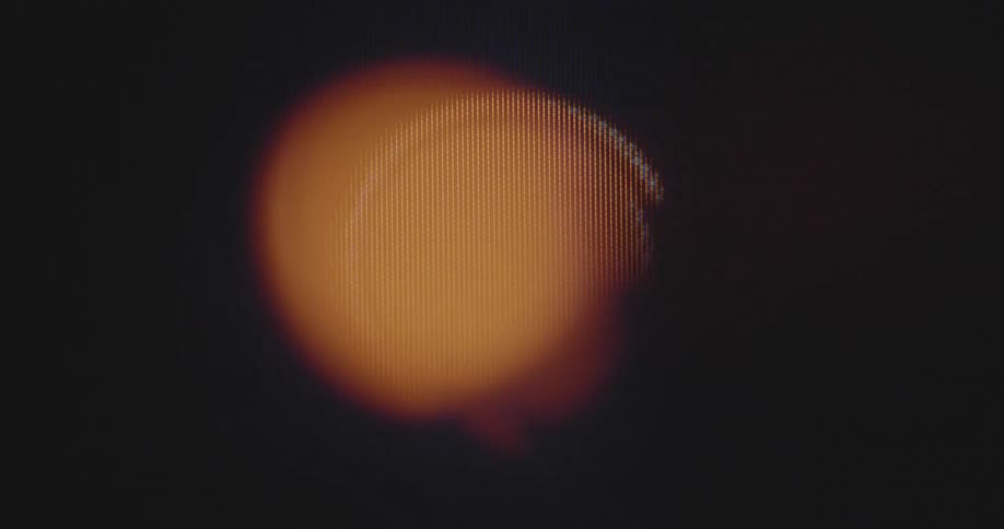 A line spins around a symmetrical orange circle shown on a pixel display as the round shape moves and changes its size while pulsating like a flashing alarm or warning signal
