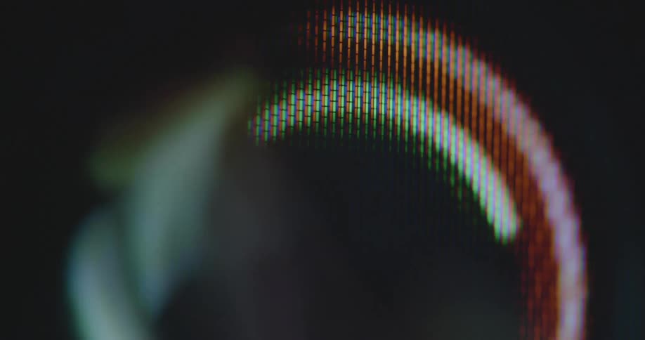 Extreme macro close up of pixelated computer screen displaying abstract loop lights effect of round colourful lines spinning in a circle looking like a digital rainbow animation