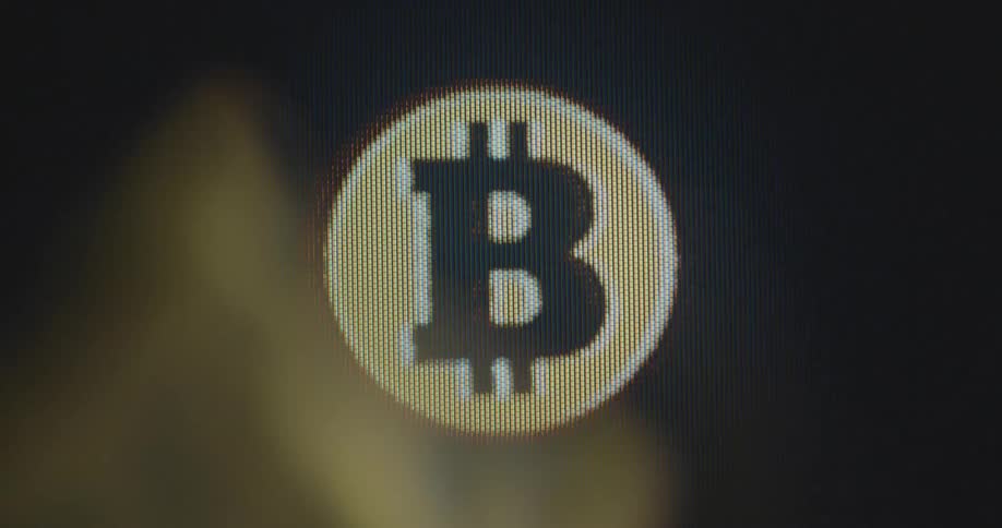 An animated orange bitcoin logo as a symbol for digital gold is displayed on a small computer screen representing the chance of financial freedom through crypto currency investment strategies