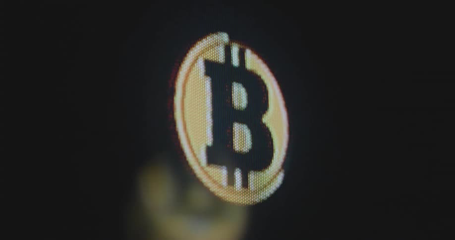 An animated circular Bitcoin cryptocurrency logo is displayed upon a pixelated computer screen representing crypto mining on the blockchain and the future of the global banking and financial system