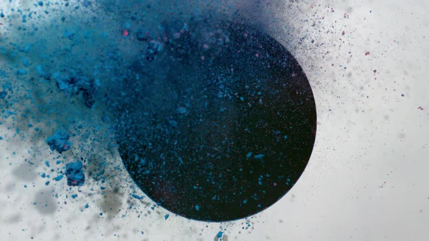 Blue and pink powders collide as they blow through a circular hole in a panel
