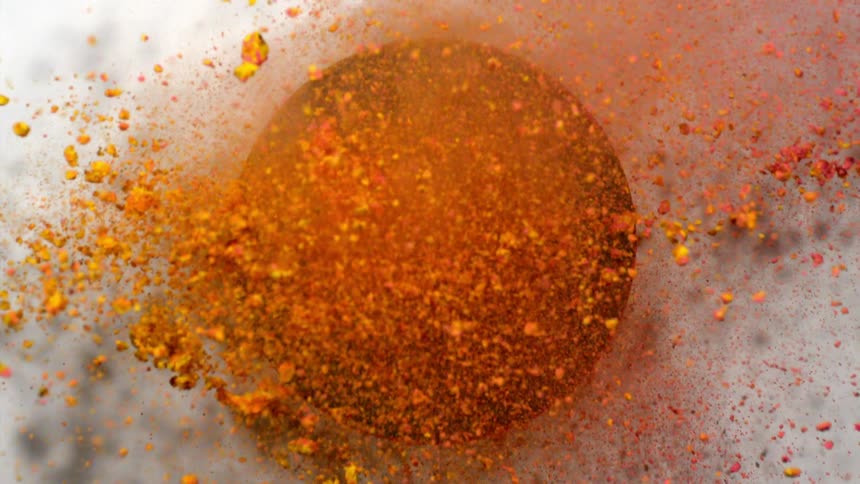 Yellow and pink powder is shot through a dark circle in a panel