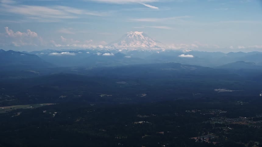 Daytime aerial view of Mount Rainier an active volcano in the Cascade Range with snow-capped peaks and partly cloudy skies in Washington during summer