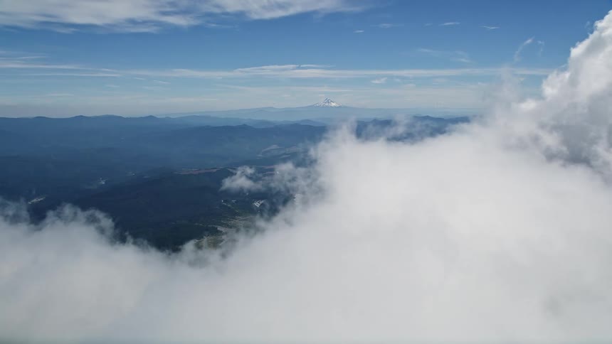 Aerial footage flies through clouds to reveal Mount Rainier in the far distance over Washington's beautiful landscape