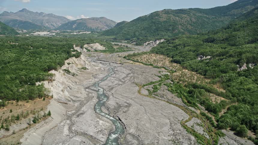 A serene aerial view of the North Fork Toutle River in Washington as the camera pans across the sediment-filled water surrounded by lush forest and scattered boulders