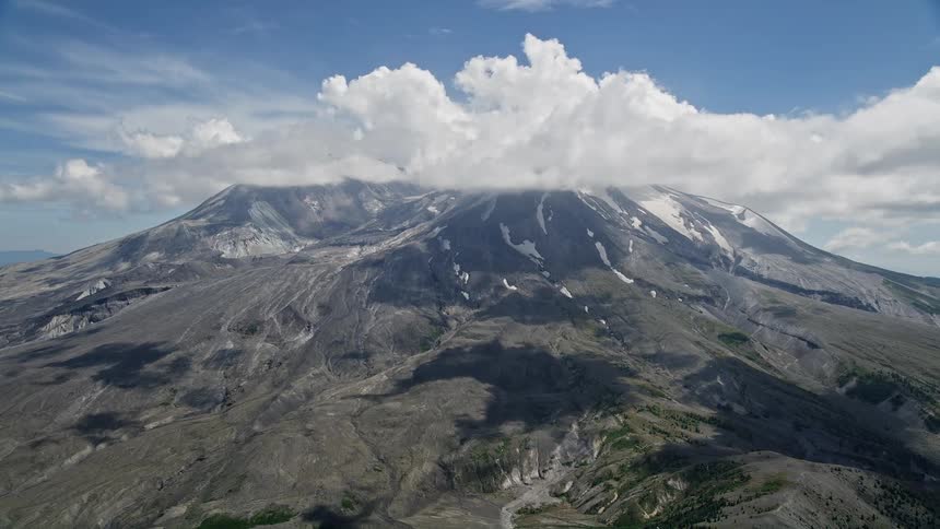 Aerial footage captures the approach to cloud-capped Mount St Helens showing patches of snow on the peaks in the scenic wilderness of Washington