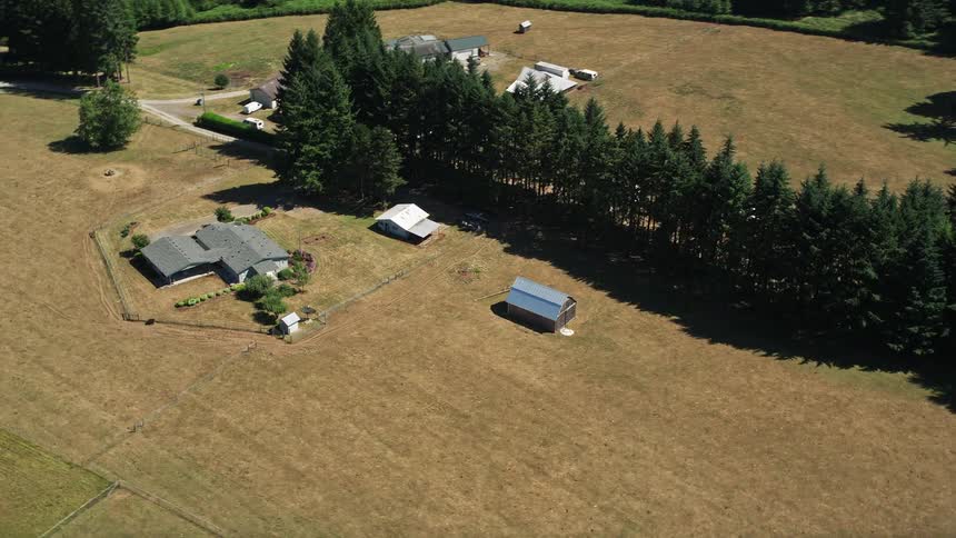Aerial footage of a small rustic barn and farmhouse surrounded by farmland and sunshine in La Center Washington during summer